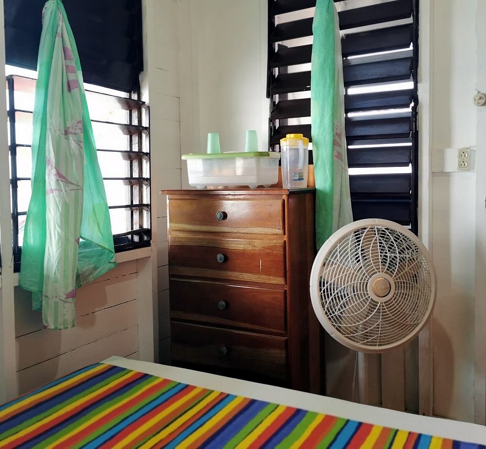 A bed, drawer and fan in the interior of a cabin
