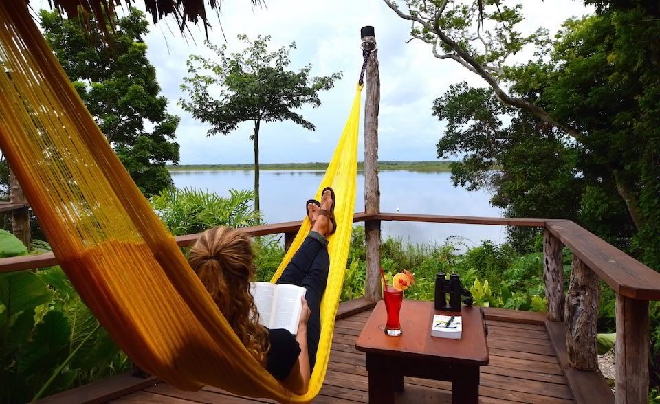 Woman reading in a hammock on the porch of a lagoon front cabana at Lamanai Outpost Lodge