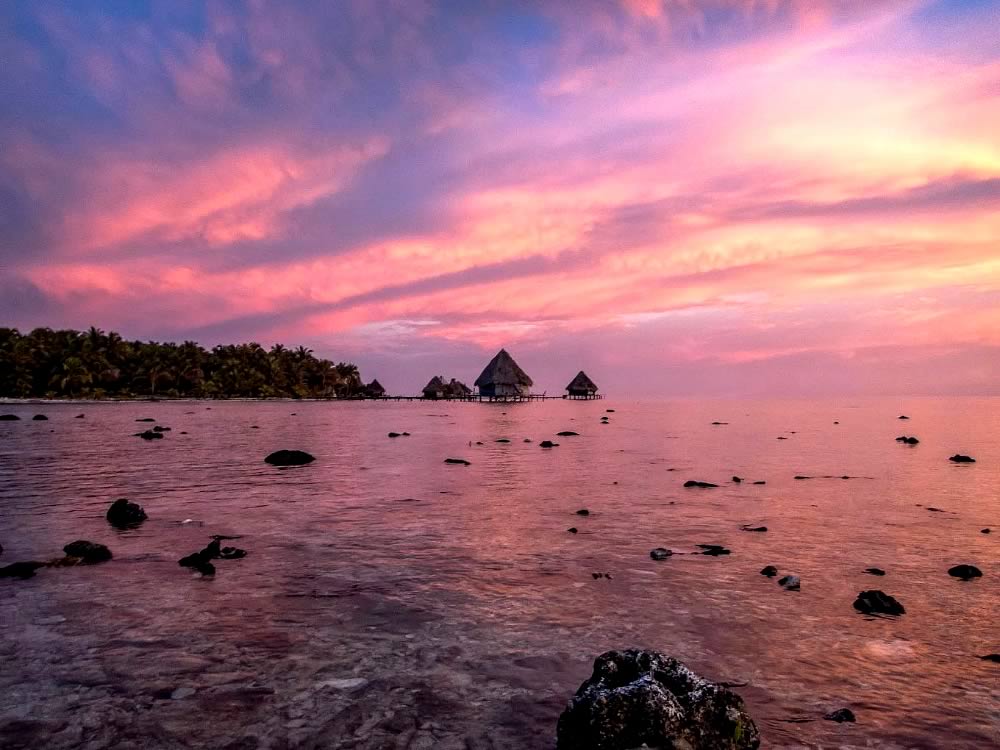 View of a cluster of overwater cabins and glittering waters with a pink sunset