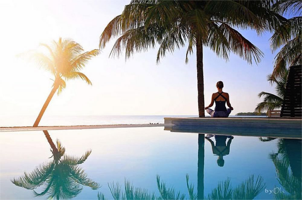 Woman doing yoga on the pool deck facing the beach